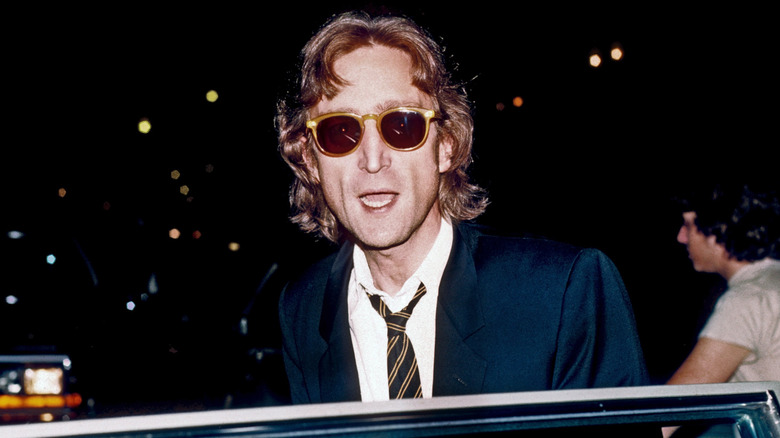 John Lennon getting into a car at night wearing sunglasses, suit, and tie