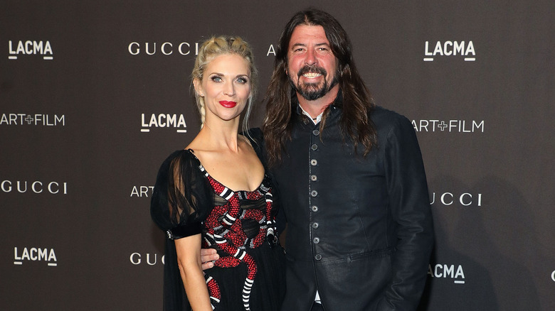 Dave Grohl in black button up jacket and Jordyn Blum in black and red dress