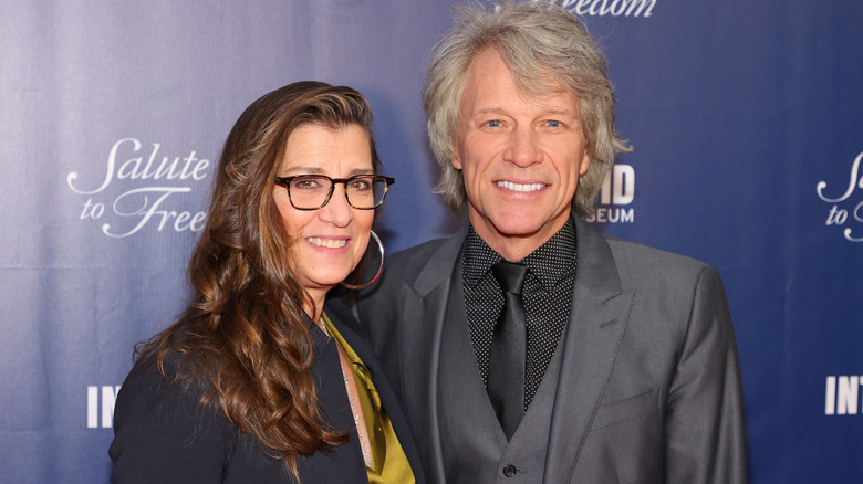 Jon Bon Jovi in gray suit with Dorothea Bongiovi in black blazer and mustard shirt wearing glsases