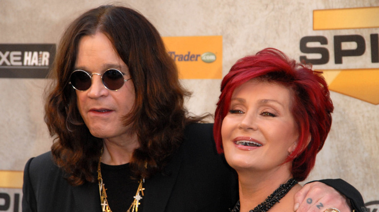 Ozzy Osbourne in black shirt and sunglasses with arm around Sharon Osbourne smiling