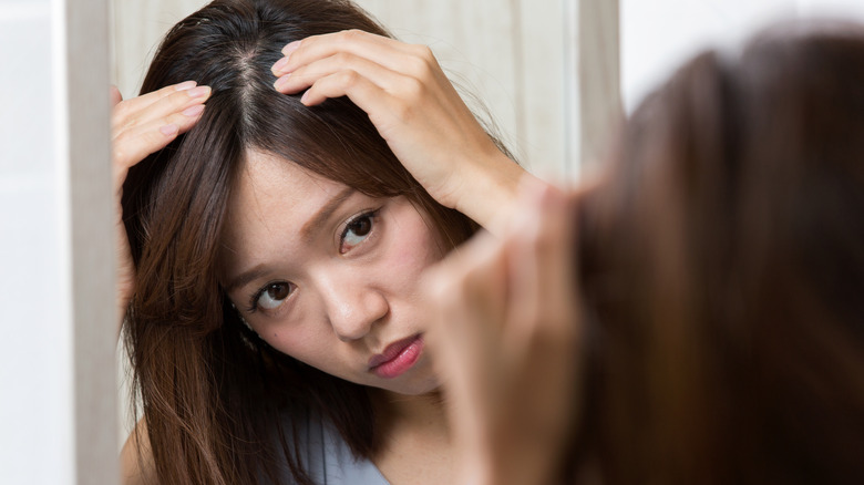 A woman looking at her scalp in the mirror