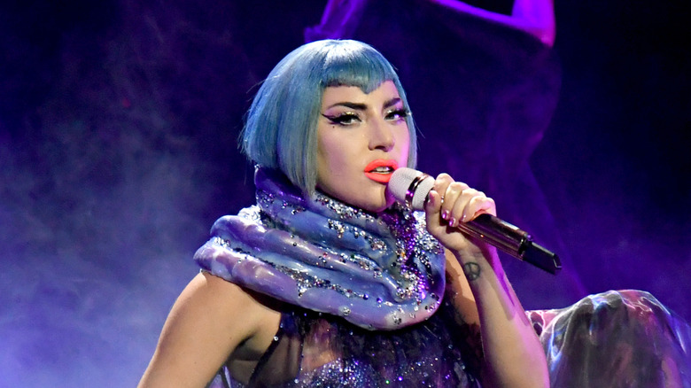 Lady Gaga performing into mic on stage wearing short blue wig