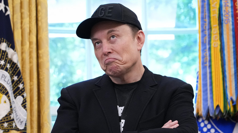 Elon Musk wearing a black baseball cap in the Oval Office