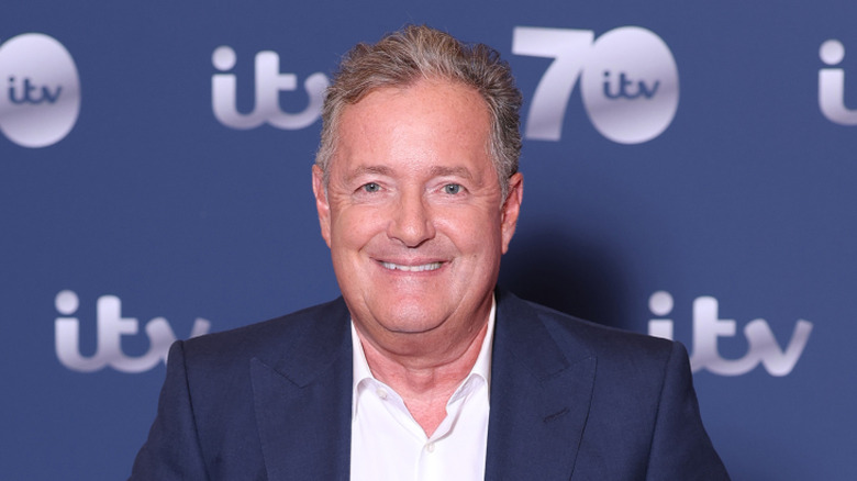 Piers Morgan posing in front of a blue background
