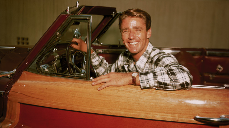A grinning Peter Lawford at the wheel of his wood-finish convertible, circa