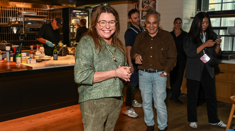Rachel Ray wearing a green outfit and standing in a kitchen and smiling