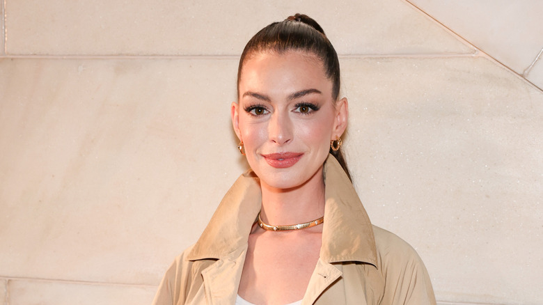 Anne Hathaway in a tan coat with hair pulled up in a ponytail