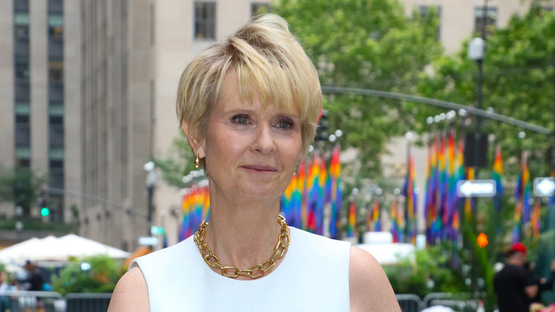 Cynthia Nixon in a white outfit with pride flags in background