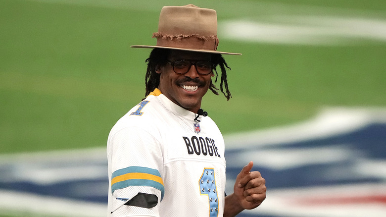 Cam Newton wearing a hat and jersey on a football field in February 2026