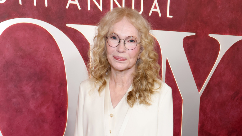 Mia Farrow standing against red background in June 2025