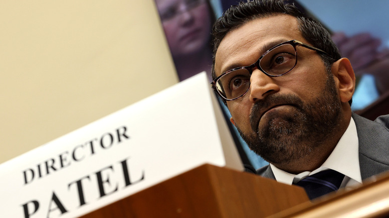 A crooked angle of Kash Patel frowning behind a desk from a low angle.