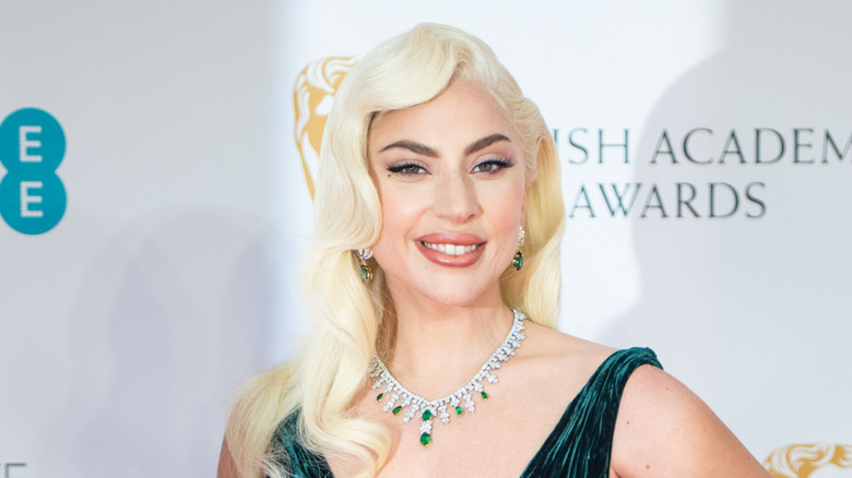 Lady Gaga getting her photo taken with platinum blonde hair and a green necklace with matching earrings