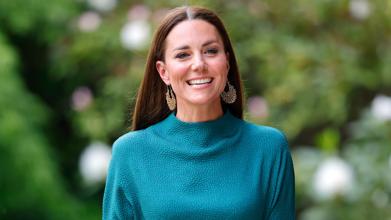 Kate Middleton with her hair in a middle part, wearing a green dress and statement earrings