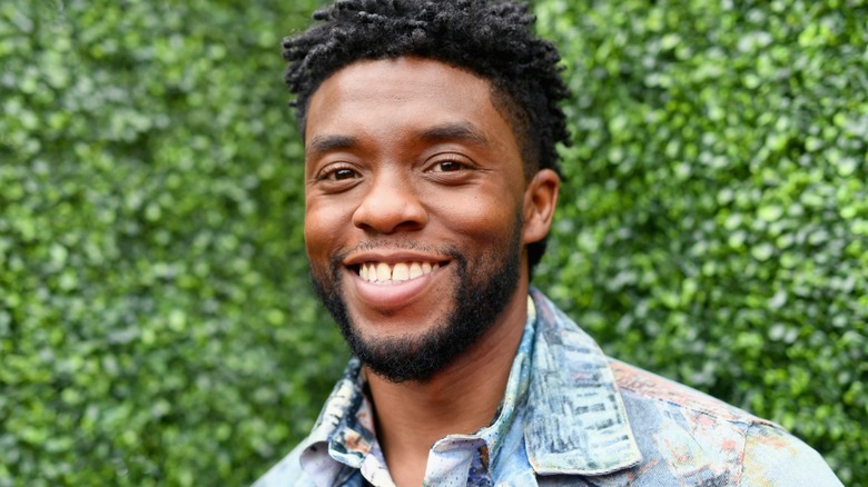 Closeup of Chadwick Boseman smiling against a hedge wall