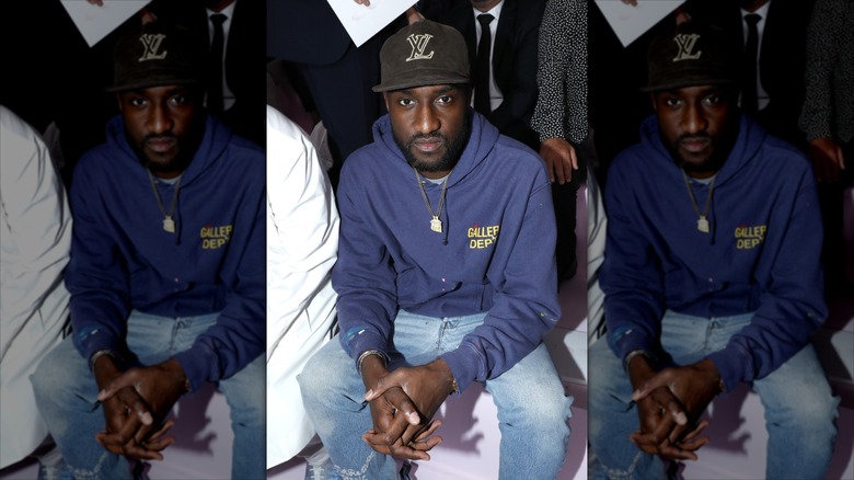 Virgil Abloh in a blue hoodie and Louis Vuitton hat sitting at a fashion show