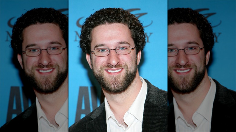 Dustin Diamond in glasses, smiling in front of a blue background