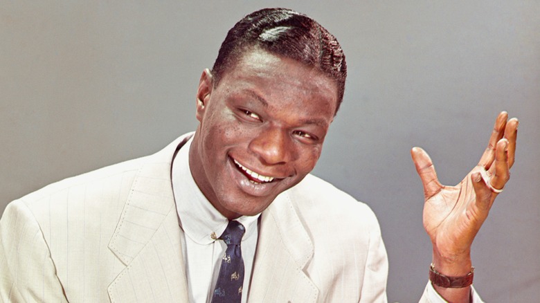 Nat King Cole in a white suit, holding up a hand