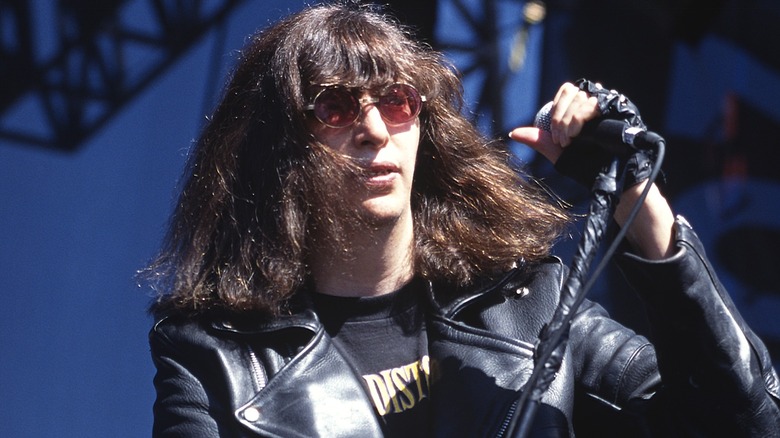 Joey Ramone performing onstage in a leather jacket and red sunglasses