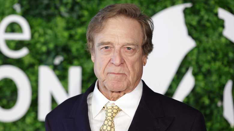 John Goodman in formals against a leafy background