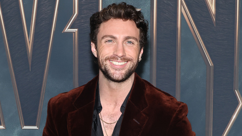 Aaron Taylor-Johnson smiling in a rust velvet coat