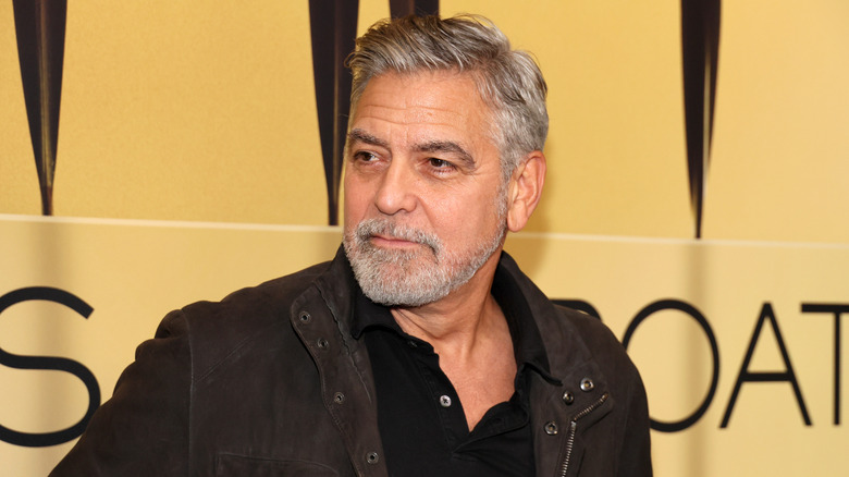 George Clooney in a brown jacket against a golden background
