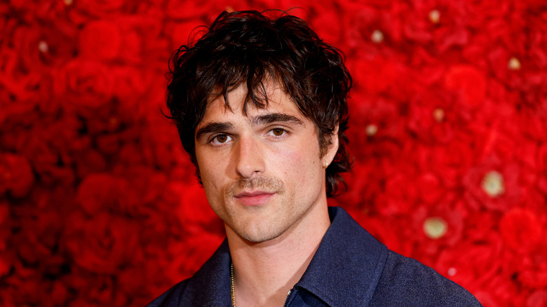 Jacob Elordi posing against a red floral background