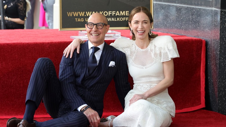 Stanley Tucci and Emily Blunt sitting and laughing during their Hollywood Walk of Fame ceremony.