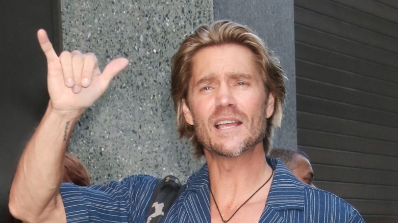 Chad Michael Murray in a blue shirt holds his right hand up in a "rock on" symbol