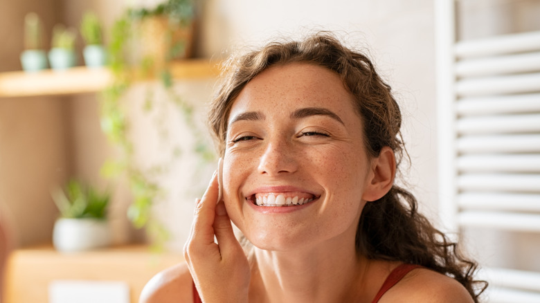 Woman using skincare products while smiling 
