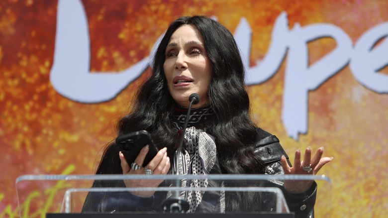 Cher holding cellphone while at podium