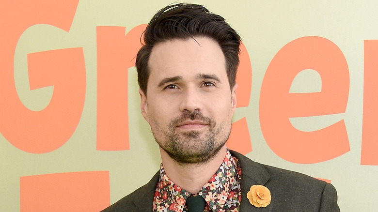 Brett Dalton slightly smiling while posing on the red carpet in a floral shirt