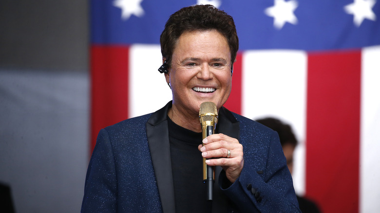 Donny Osmond holding a golden microphone and smiling at a concert.