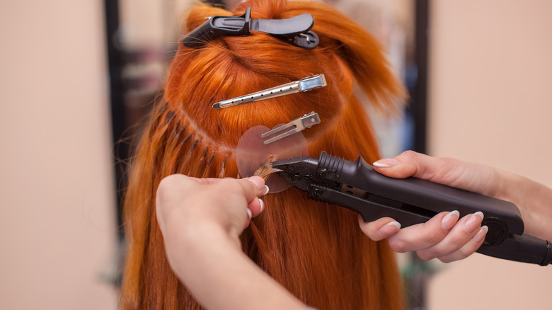 Hair extensions being applied to red hair