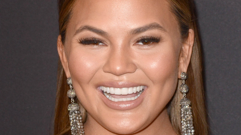 Chrissy Teigen smiling with long earrings