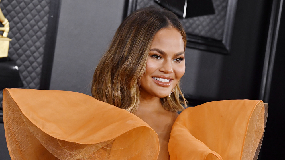 Smiling Chrissy Teigen in an orange gown 