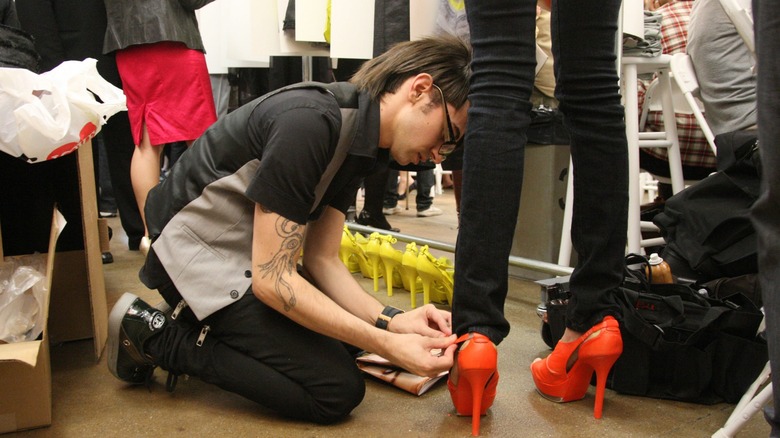 Christian Siriano kneeling backstage at a fashion show, putting the finishing touches to a model's heels