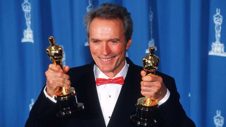Clint Eastwood smiling and holding up two Oscars in 1993
