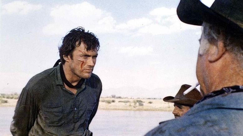 Clint Eastwood with hands behind his back and cuts on his face as he stands in front of two cowboys in Hang 'Em High