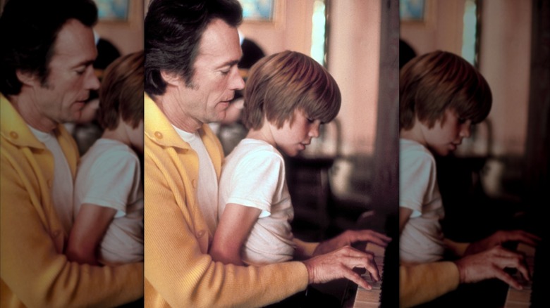 A younger Clint Eastwood playing the piano with his son on is lap