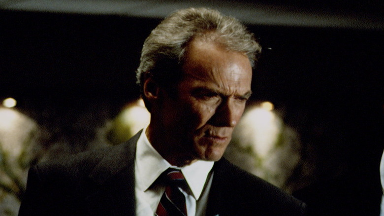 Clint Eastwood wearing a suit and looking downward frowning "In the Line of Fire"