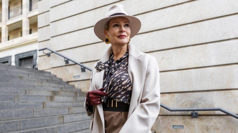 Stylish older woman in cute outfit and hat posing on steps outside