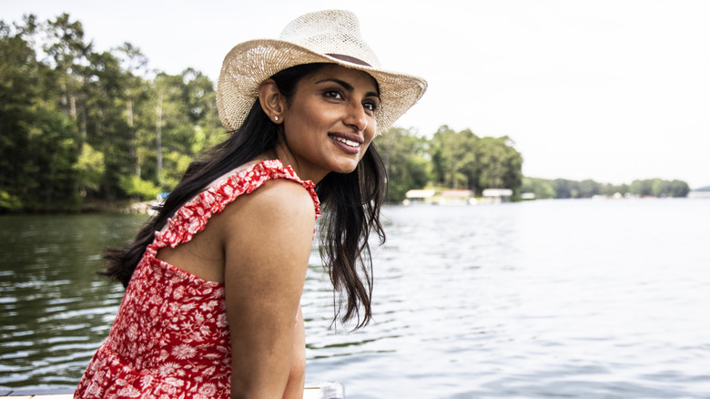 Portrait of woman sitting on dock at lake wearing hat and red dress