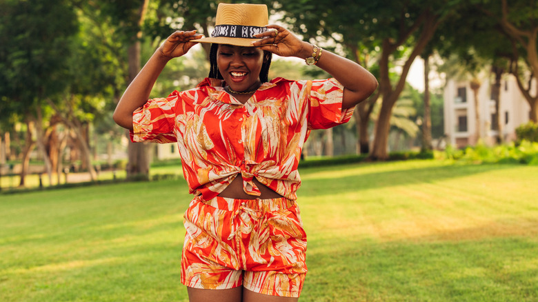 Woman smiling holding hat and wearing red print two-piece shorts and short in green park area