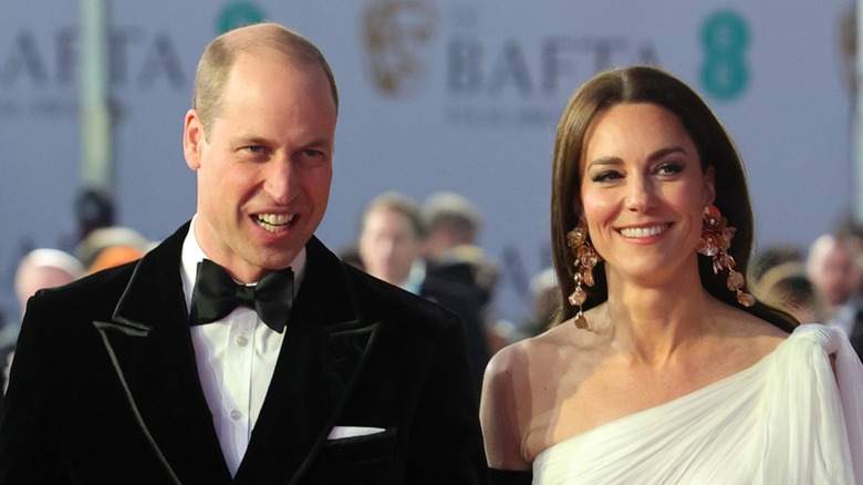 A smiling Prince William and Princess Catherine wearing elaborate hats