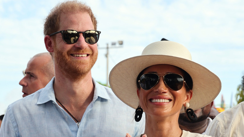 A smiling Prince Harry and Meghan Markle wearing sunglasses
