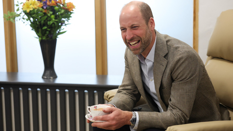 Prince William laughing while holding a cup of tea.