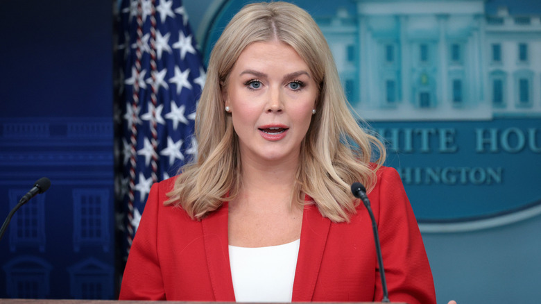Karoline Leavitt wearing a red suit while addressing reporters