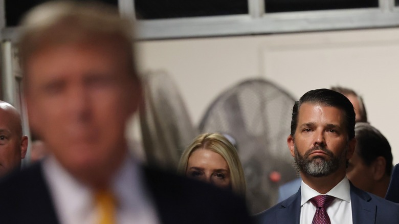 President Donald Trump blurry in the foreground, with Donald Trump Jr. in focus in the background looking at his father