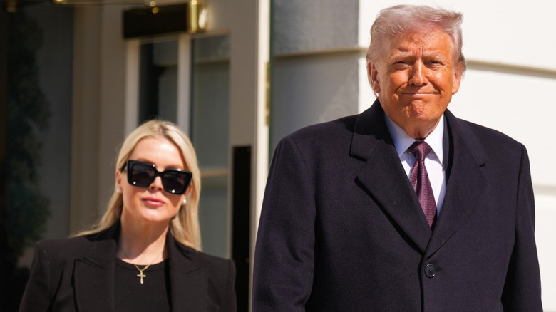 Karoline Leavitt wearing sunglasses and walking slightly behind Donald Trump