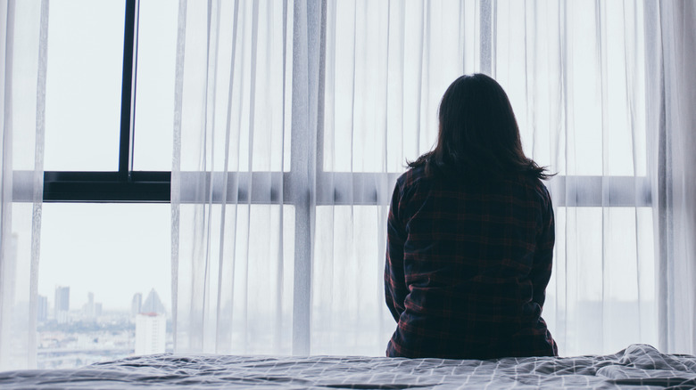 woman sitting alone on a bed with her back to the camera